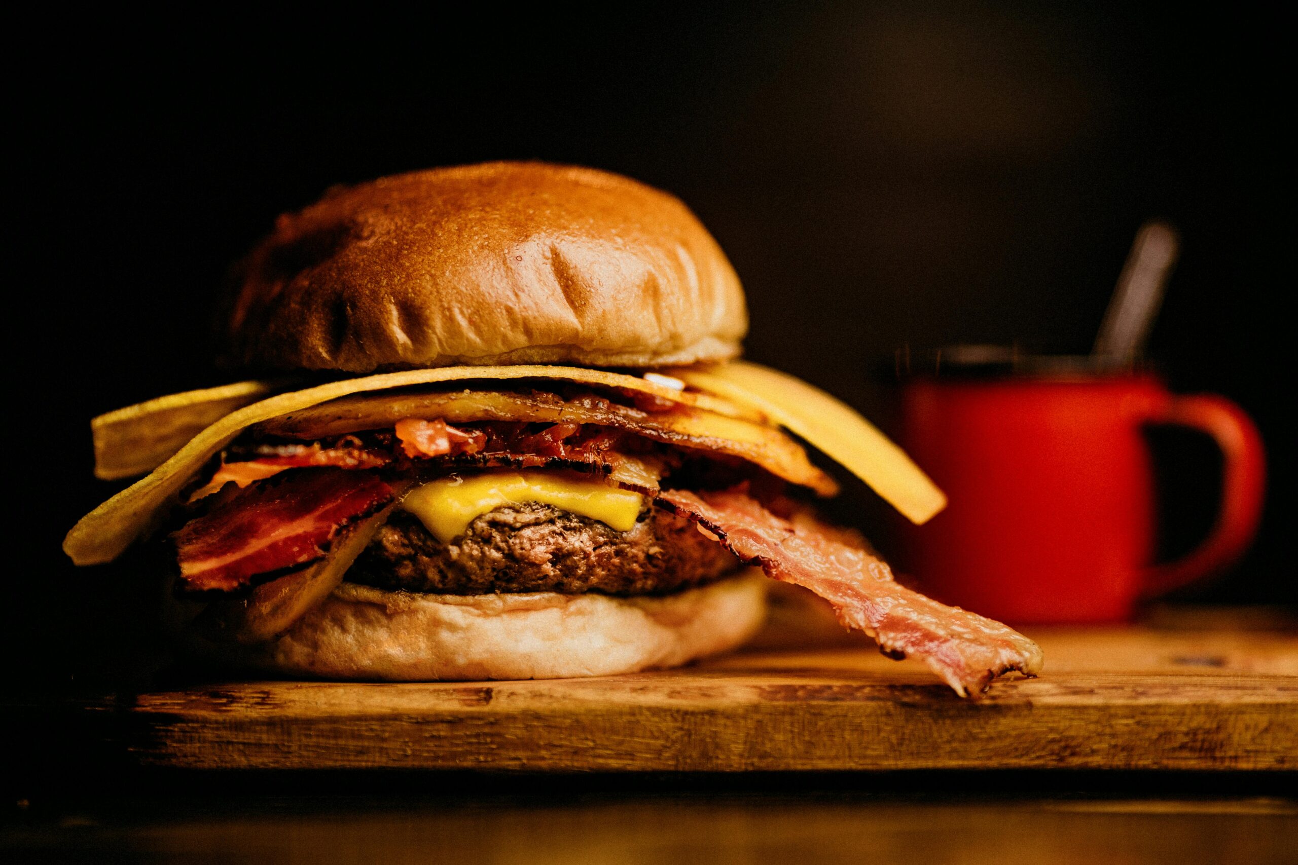 Close-up of a gourmet bacon cheeseburger with a side of crispy fries on a wooden board.